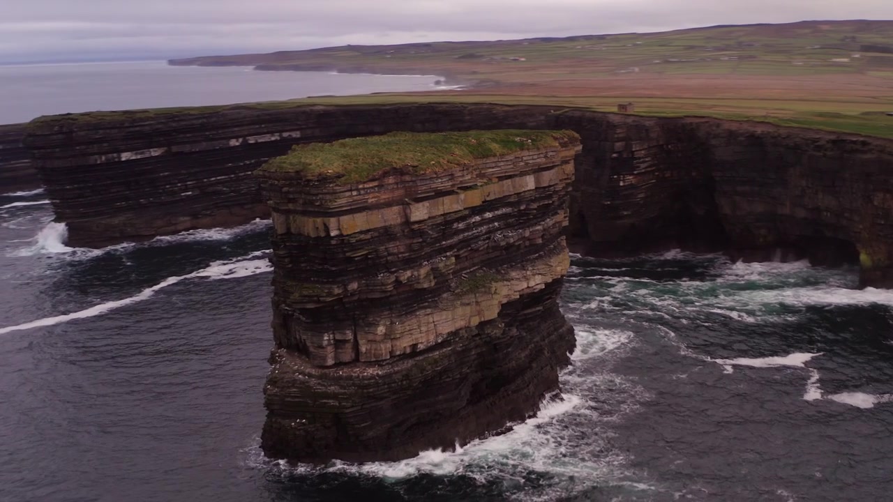 Aerial orbit clockwise around Dun Briste sea stack by Downpatrick Head peninsula with ocean waves crashing against the cliffs