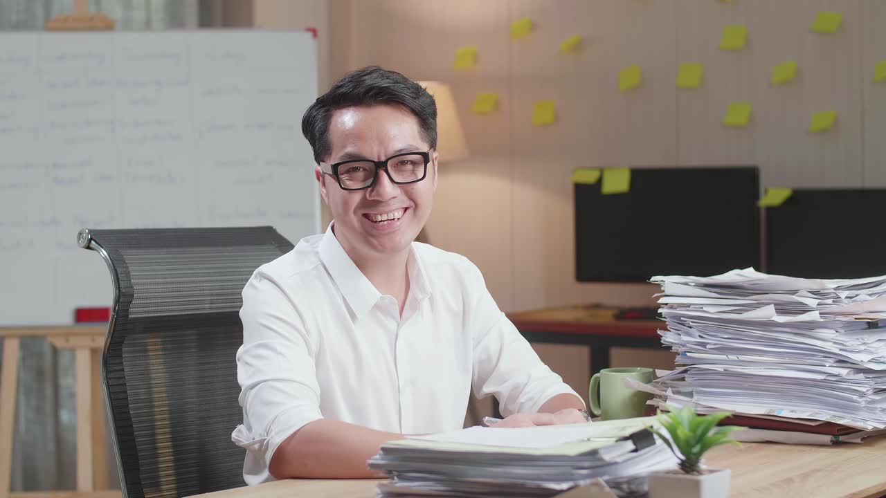 Asian Man Smiling To Camera While Working With Documents At The Office