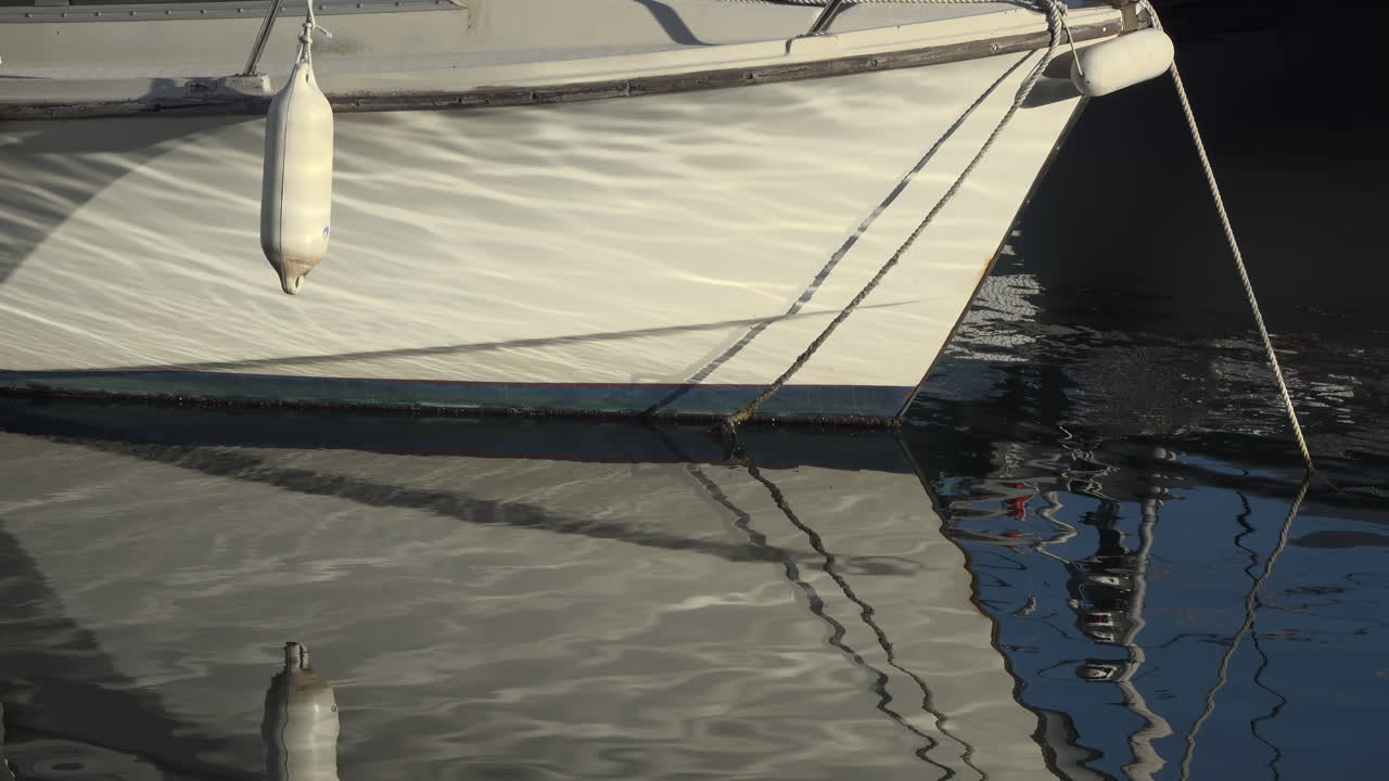 Close up of the side of a boat docked in the water, with fenders hanging from its hull