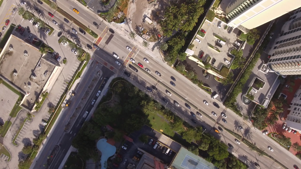 Spinning top-down drone view descends over a busy Miami street with traffic.