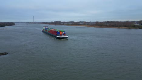 aerial dolly towards cargo container ship approaching along beneden merwede on overcast day