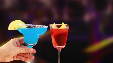 two vibrant cocktails, blue and red, are raised in a celebratory toast against a colorful, blurred background