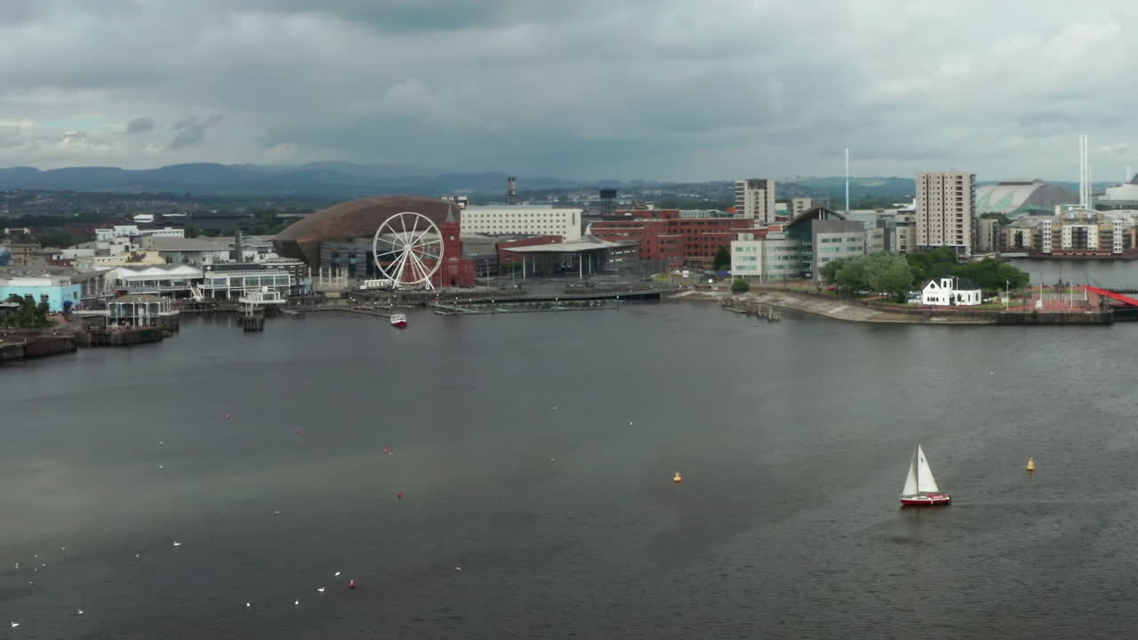 Narrow Static Aerial Shot of Sailboat Navigating Cardiff Harbour on a Cloudy Day with the Quayside in the Distance
