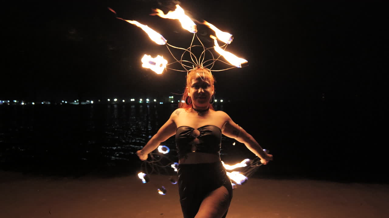 A young woman dancing with her fire ring at night during her show in front of the pier. Slowmotion