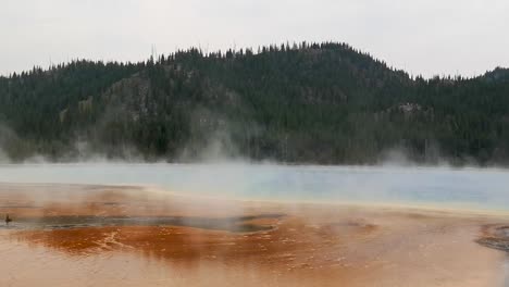 Gran-Manantial-Prismático-Con-Vapor-En-El-Aire-Y-Paisaje-Montañoso-En-El-Parque-Nacional-De-Yellowstone-Wyoming,-Estados-Unidos