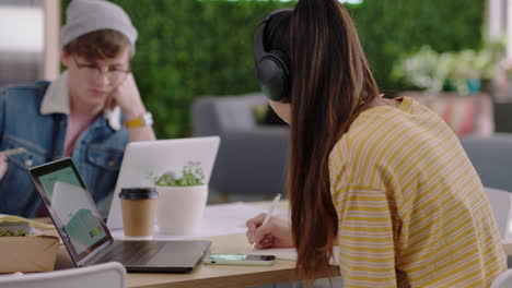 beautiful young asian woman student using laptop computer working on creative project browsing online research writing notes enjoying study listening to music wearing headphones in trendy office