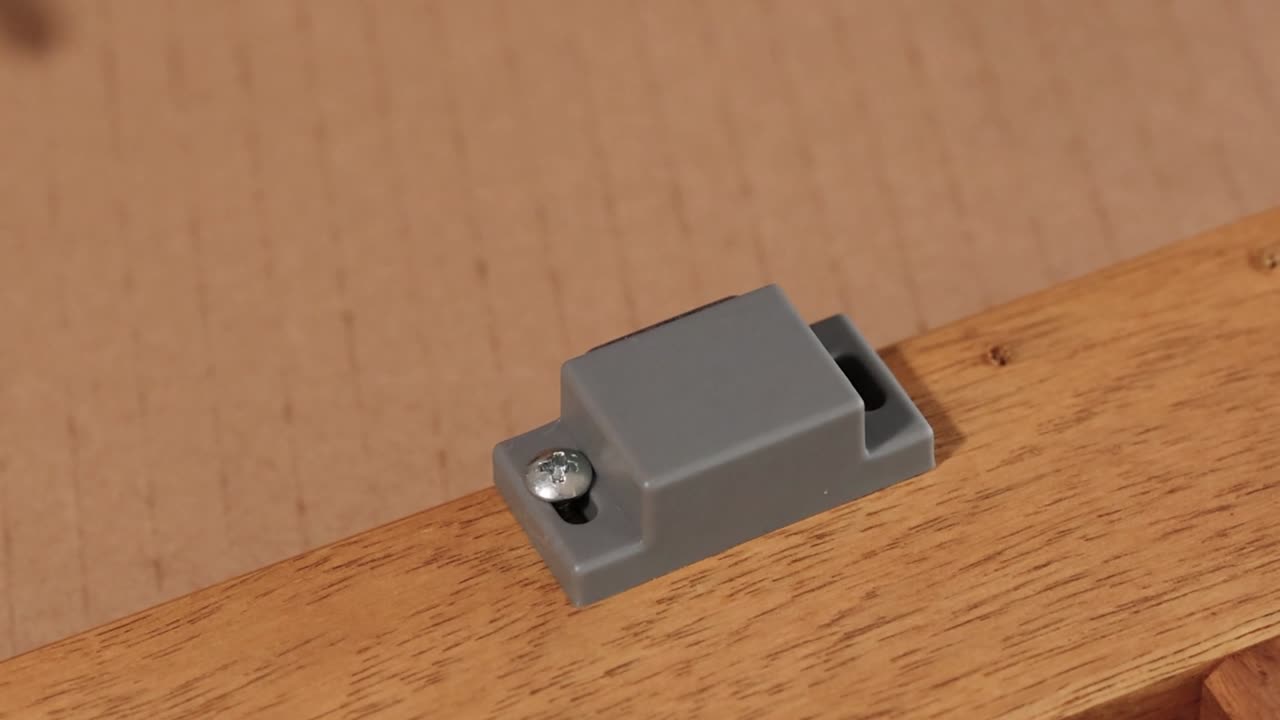 Una persona coloca con cuidado un cierre magnético e introduce un tornillo en un mueble de madera