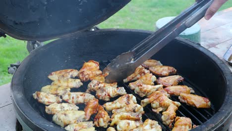 mujer usando tenazas para voltear alitas de pollo cocinando en una parrilla de cerámica estilo kamado con sonda de temperatura digital