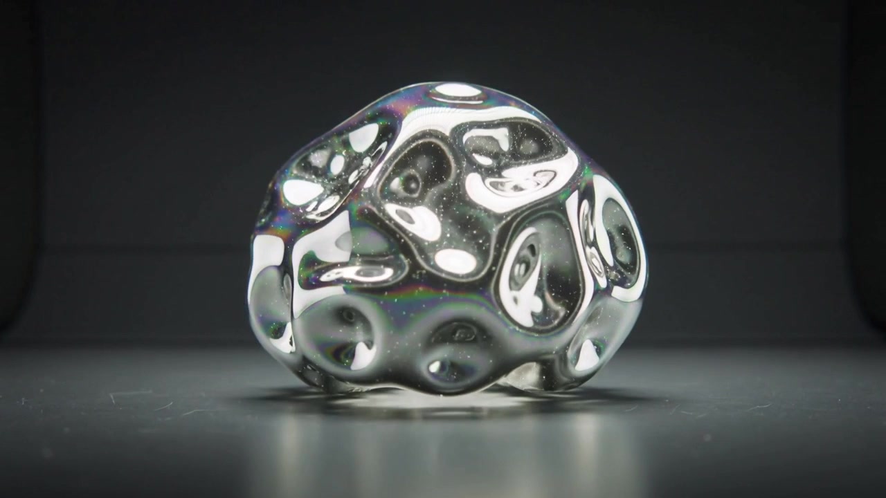 Reacting to softbox light, morphing sphere deforming on dark gray tabletop with speckles