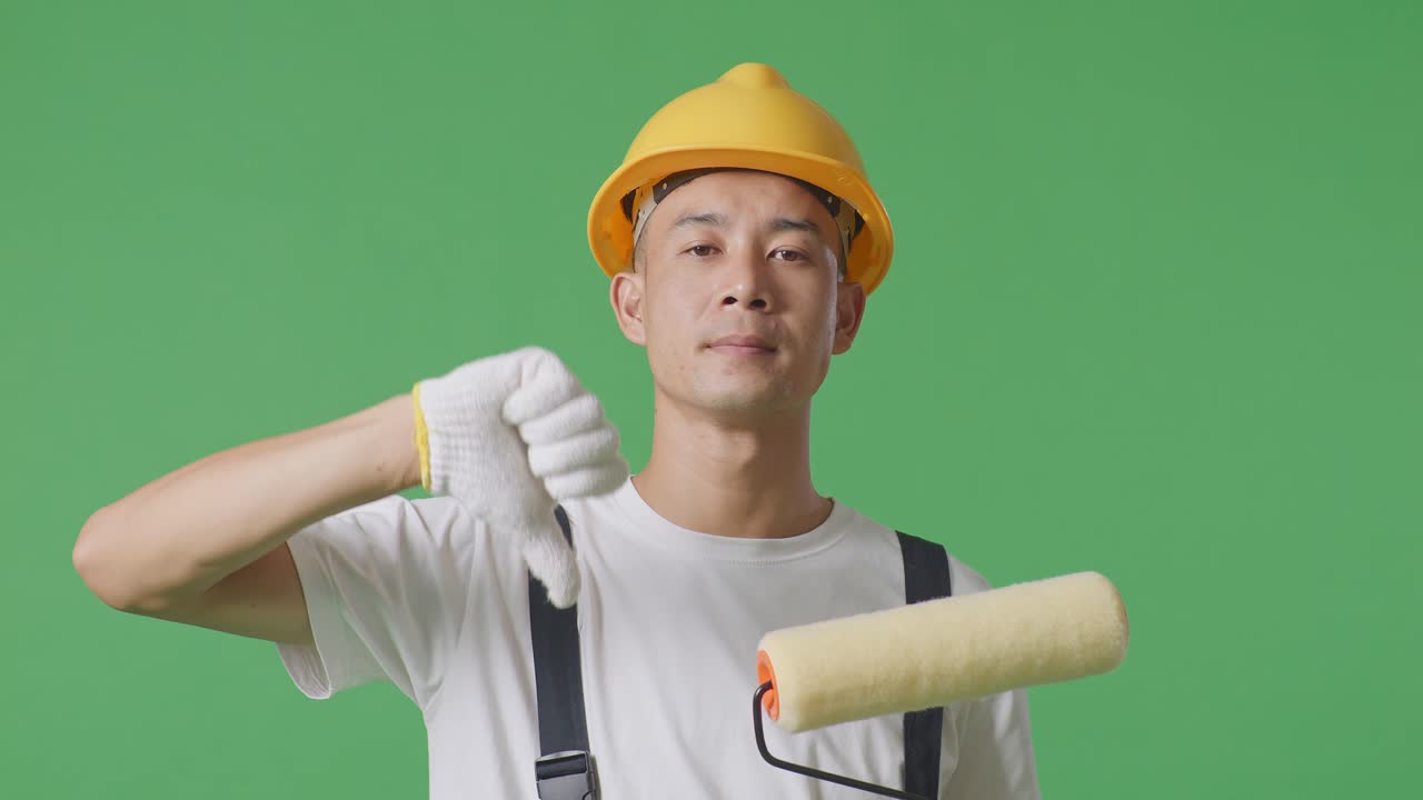 Close Up Of Asian Man Painter Wearing Safety Helmet Showing Thumbs Down Gesture To Camera While Standing In The Green Screen Background Studio