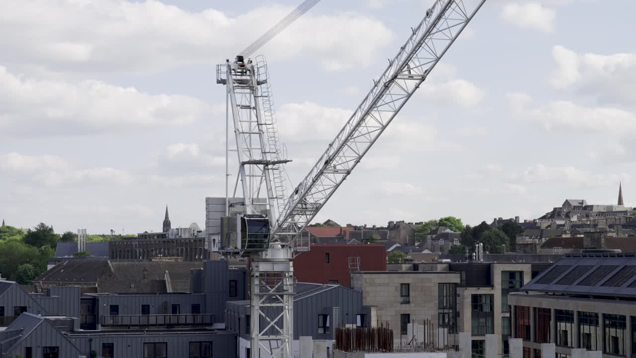 Aerial static shot of white working crane in a construction site with buildings in the background