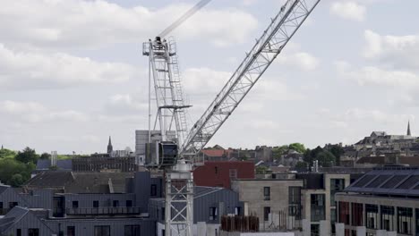 aerial static shot of white working crane in a construction site with buildings in the background
