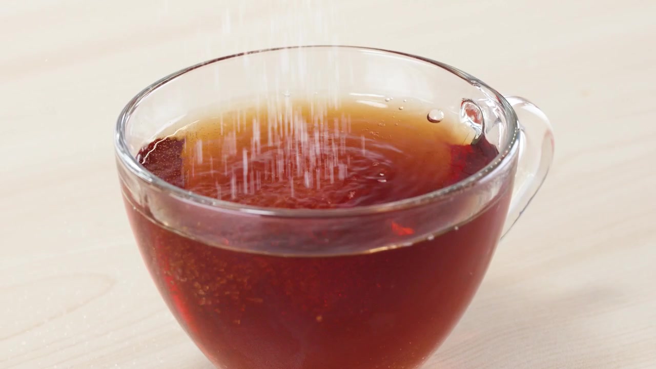 木製のテーブルの上で、白いグラニュー糖が熱い紅茶の入ったガラスカップに注がれている様子
