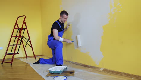 happy male worker is painting wall. professional young man with paint roller having fun in the apartment. room painting job. renovation home concept.