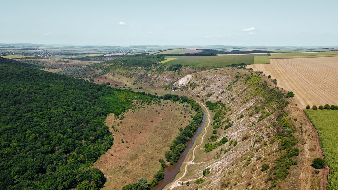 Aerial drone view of a valley with floating river, hill slopes, greenery and fields in Moldova
