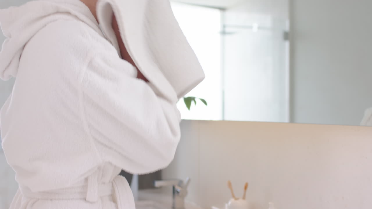 Drying face with towel, woman in bathrobe enjoying spa treatment at home