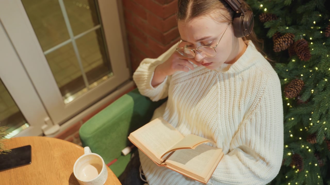 Junge Frau mit Kopfhörern liest ein Buch am Weihnachtsbaum