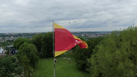 Flag-of-Kaunas-city-waving-on-cloudy-moody-day,-close-up-aerial-view