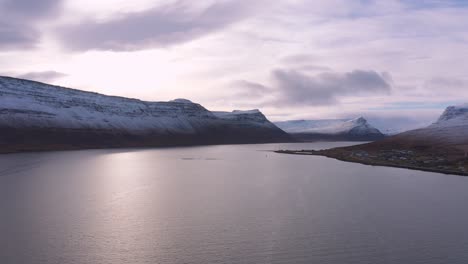 aerial view showing a serene arctic ocean surrounded by snow capped mountains on a lovely cloudy day during extreme winters, icelandic westfjords