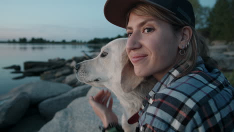 mujer sonriente abrazando a un lindo perro por el lago