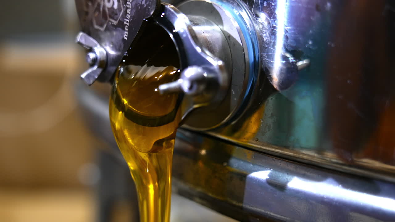 Opened mouth of a honey extracting machine with liquid product flowing from it. Freshly extracted organic food close up.