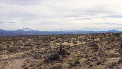 aerial, speed ramp to pan along an empty desert road past huge boulder formation against the background of the snow-capped four peaks, scottsdale, arizona