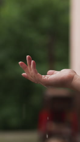 woman hand catches raindrops outdoors closeup. lady holds elegant arm under warm falling raindrop at house backyard. beauty of spring weather