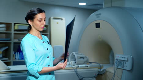 Woman specialist with x-ray photo. Portrait of a female doctor looking at scanning image on the background of MRI machine.