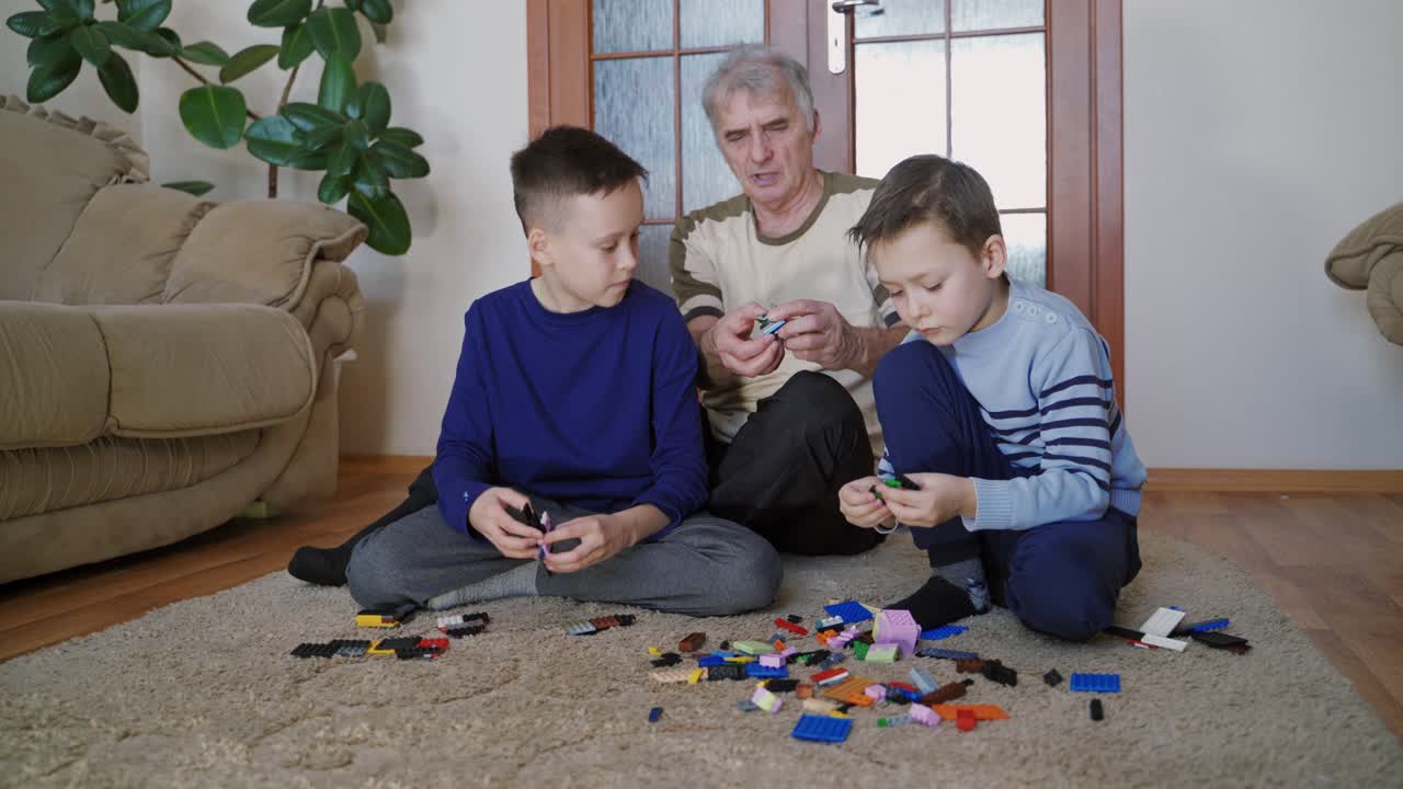 Favorite grandfather is involved in collecting the constructor, surrounded by two grandchildren in the room at his leisure. A joint pastime.