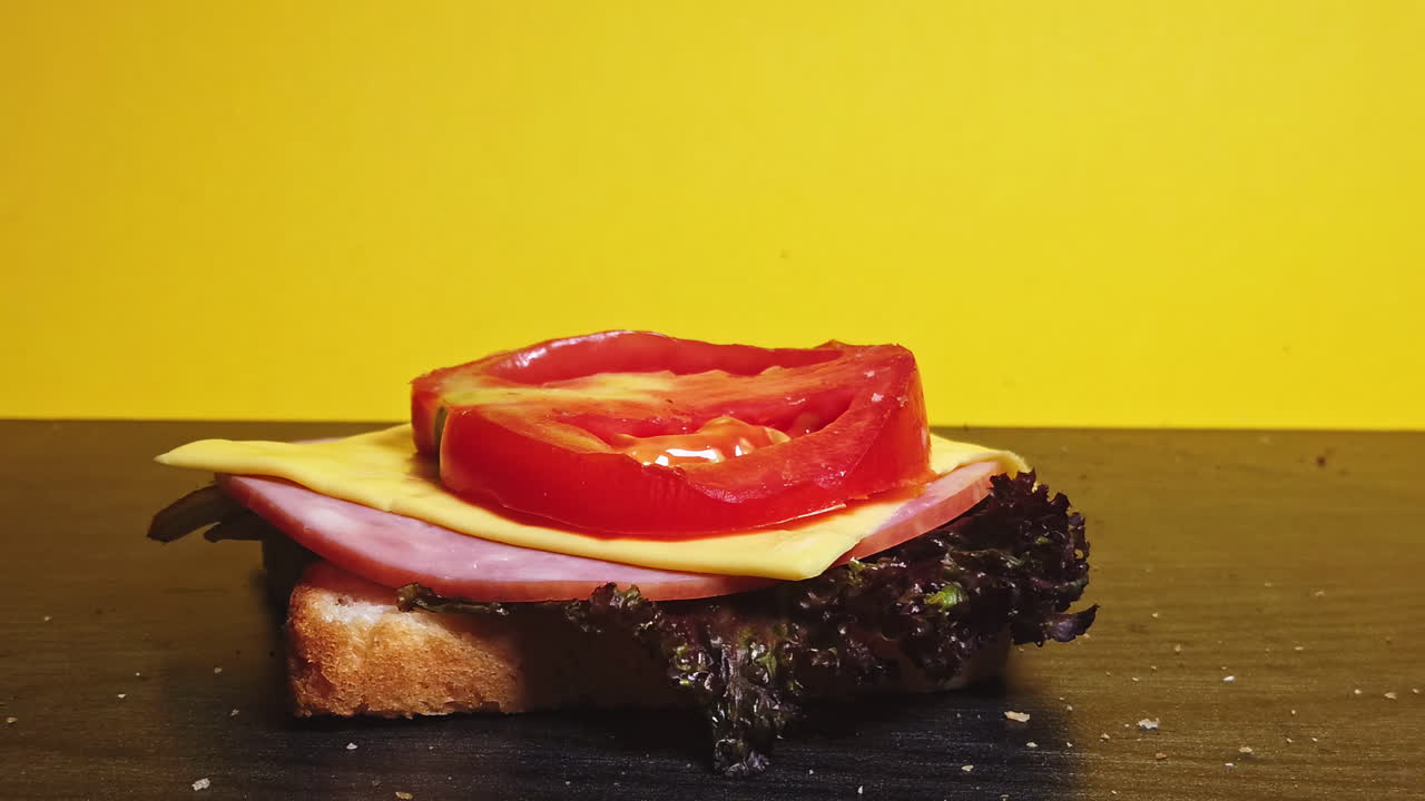 Close-up shot of a sandwich falling in layers in front of a yellow background