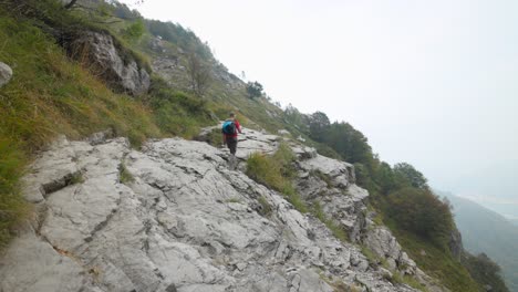 Un-Hombre-Caucásico-Camina-Sobre-Rocas-En-La-Montaña-En-Los-Alpes-Italianos-Con-Camisa-Roja-Y-Mochila