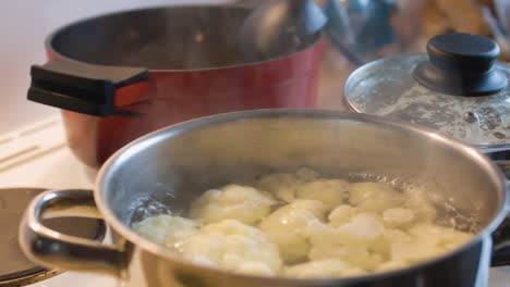 cauliflower boiling in a shiny metal pot with a cloud of steam overhead