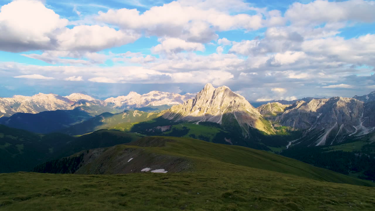 Luftaufnahme über eine üppig grüne Wiese mit Blick auf eine spektakuläre, zerklüftete Dolomitenlandschaft