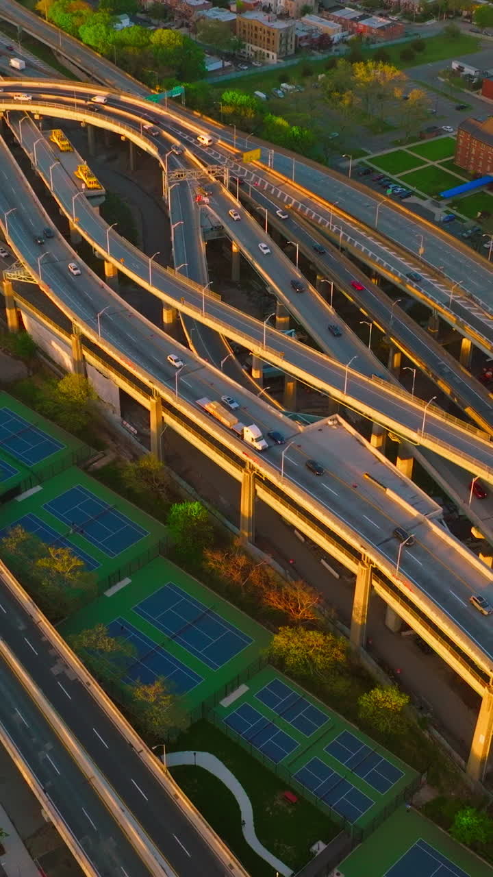 Numerous motorways crossing each other and intertwining. Tennis courts located between the roads. Top view. Vertical video