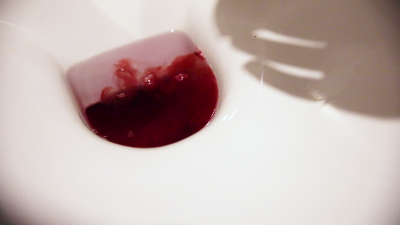 Blood flowing in the toilet, shadow of female hand emtyping menstrual cup in white toilet.