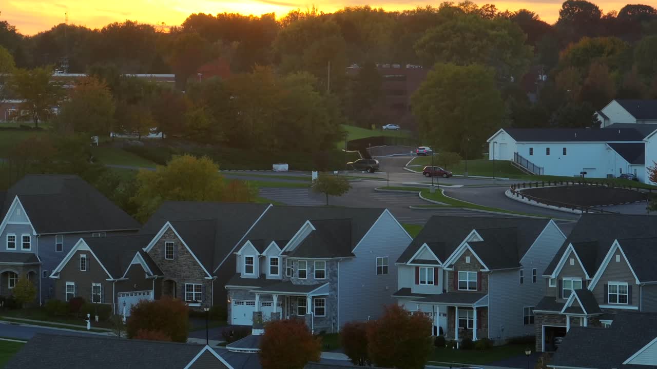 puesta de sol sobre un vecindario suburbano con grandes casas uniformes y árboles de otoño