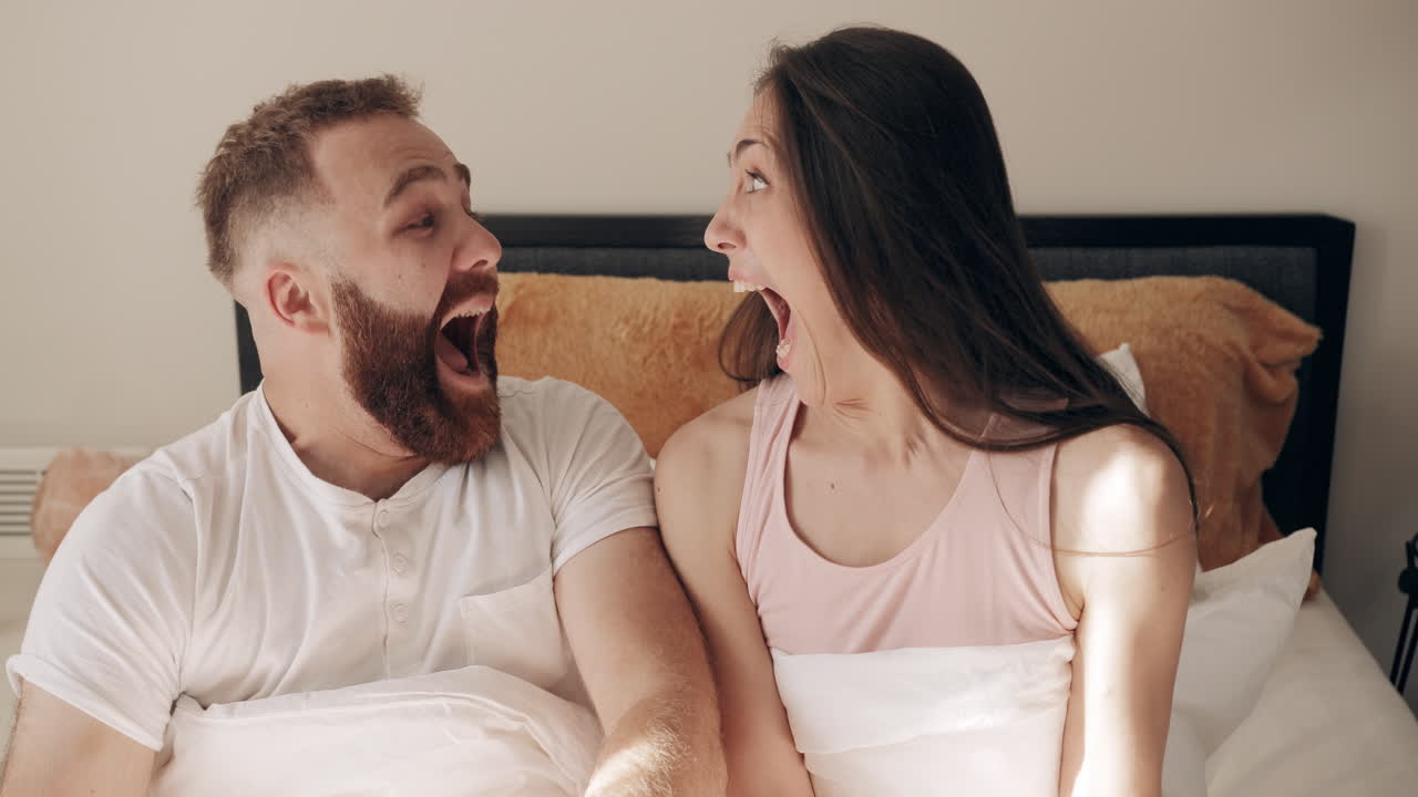 Young Couple Wakes Up in Bed with Shocked Expressions