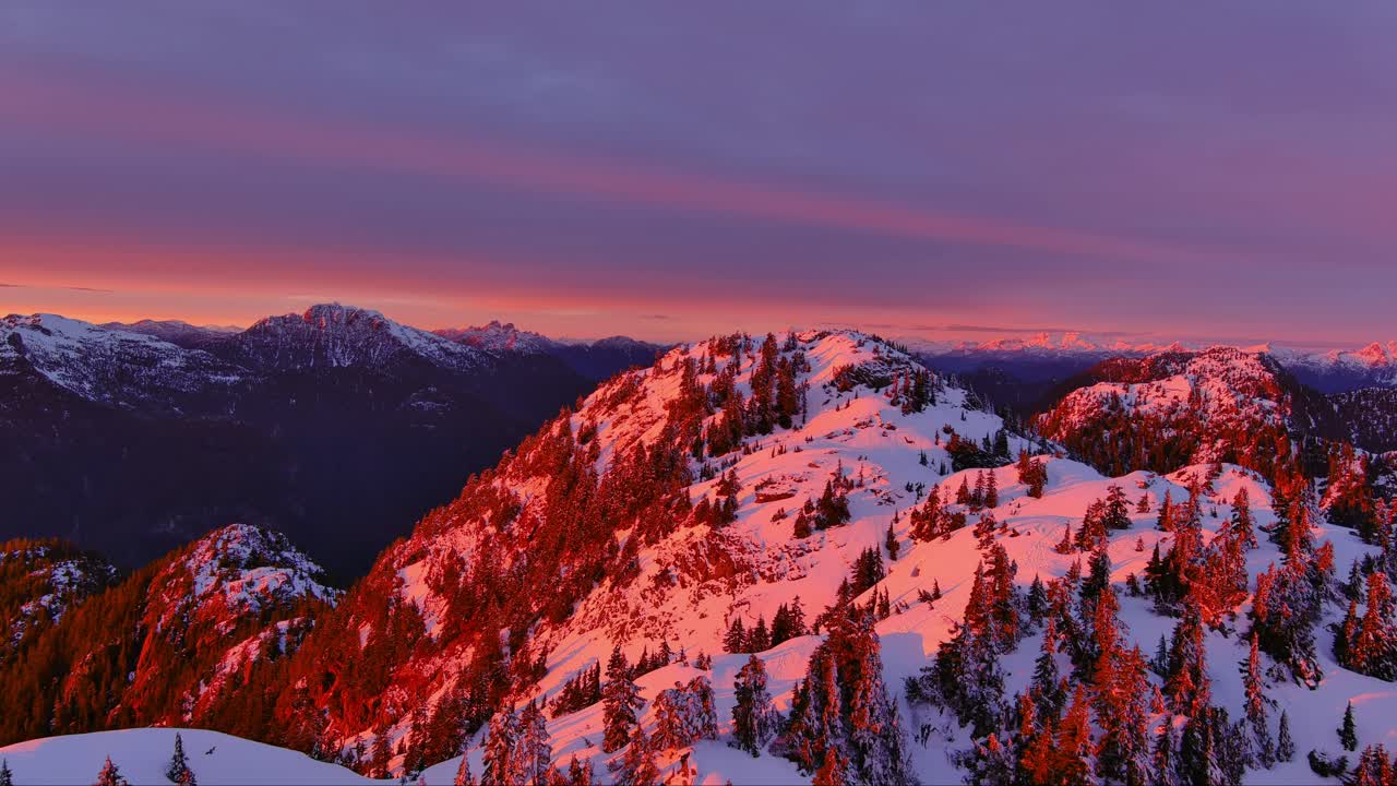Cime montuose innevate, cielo al tramonto drammatico e colorato. Alberi, paesaggio montano invernale. Nuvoloso, riprese aeree cinematografiche. Columbia Britannica, Canada.