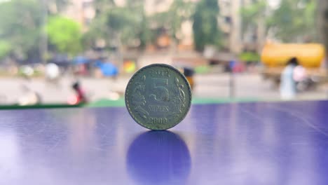 A-Five-rupees-Indian-Currency-coin-kept-on-table-with-Indian-street-background-in-Depth-of-Field,-Business,-finance,-industrial-conceptual-background-video