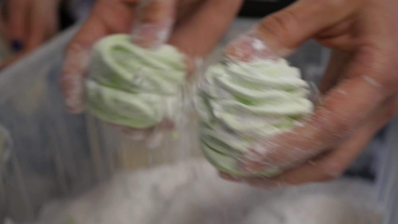 manos sosteniendo malvaviscos verdes salpicados de azúcar en polvo