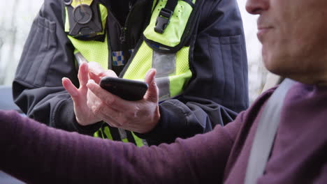 Nahaufnahme-Eines-Männlichen-Fahrers,-Der-Von-Einer-Verkehrspolizistin-Angehalten-Wird,-Die-Sich-Notizen-Auf-Dem-Mobiltelefon-Macht