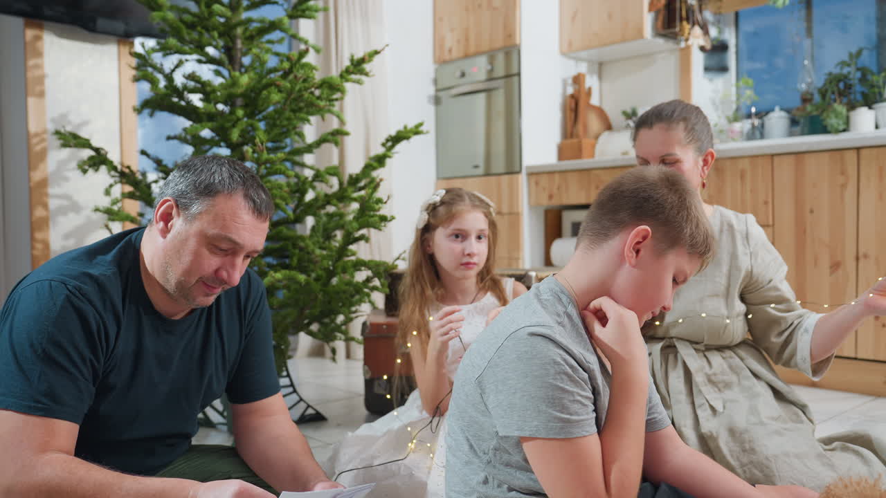 Mom and kids playing with Christmas lights while dad focuses on going through paper, enjoying family time together during holiday season, surrounded by decorations and Christmas tree