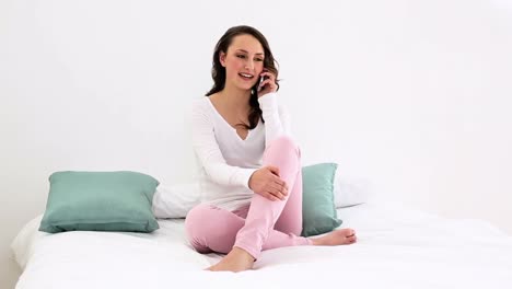 mujer sonriente sentada en la cama hablando por teléfono