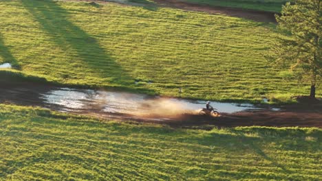 Luftaufnahme-Eines-Motocross-Rallyefahrers,-Der-Schlamm-Auf-Einer-Unbefestigten-Strecke-Auf-Einer-Grünlichen-Wiese-Spritzt