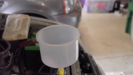 Man-pours-coolant-from-jug-into-radiator-using-large-funnel-in-garage