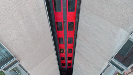 aerial tilt up of metal and glass elevator with red and black details in modern concrete building