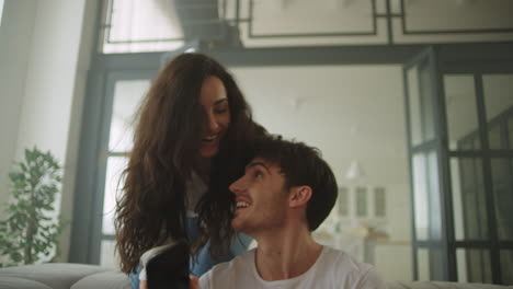 Joyful-woman-jumping-on-sofa-and-hugging-man