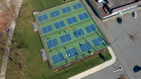 birds eye view of tennis players in a city park, drone truck left past the sports courts