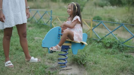 a pregnant mother and her young daughter enjoy playful time together at a playground in the park, surrounded by trees and greenery