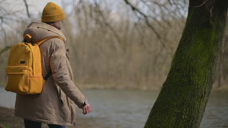 a young girl in a yellow wool cap and a yellow backpack walks through the forest towards the lake 1